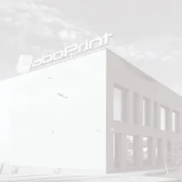 Budynek drukarni z dużym logo na dachu, widok z dołu w pochmurny dzień.