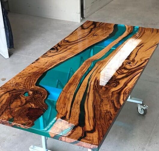 Stół z drewna egzotycznego z żywicą epoksydową w kolorze turkusowym, na metalowej podstawie z kółkami.