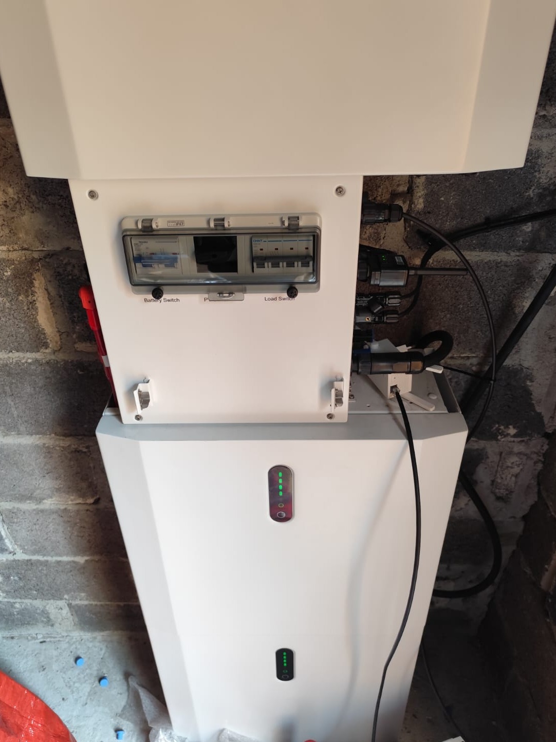 Biały moduł z przełącznikami i diodami LED zamontowany na szarej, ceglanej ścianie, widoczne kable i elementy instalacji.