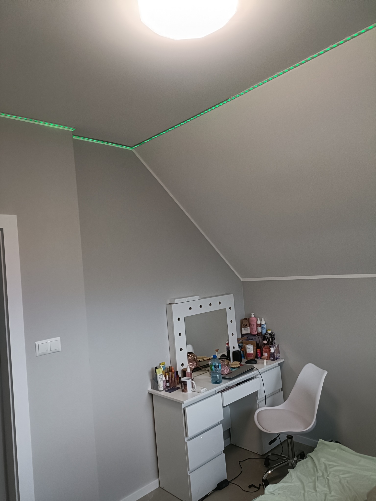 Pokój z szarą ścianą, białym biurkiem z lustrem do makijażu i zielonym oświetleniem LED na suficie.