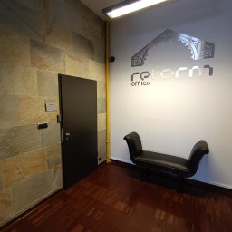 KANCELARIA ADWOKACKA ADWOKAT NORBERT PODDĘBSKI - Wnętrze biura z kamienną ścianą, ciemnymi drzwiami, drewnianą podłogą, czarną ławką i logo firmy na białej ścianie.