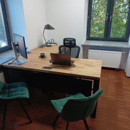 KANCELARIA ADWOKACKA ADWOKAT NORBERT PODDĘBSKI - Nowoczesne biuro z drewnianym biurkiem, dwoma zielonymi krzesłami, laptopem, monitorem i niszczarką dokumentów przy oknie.