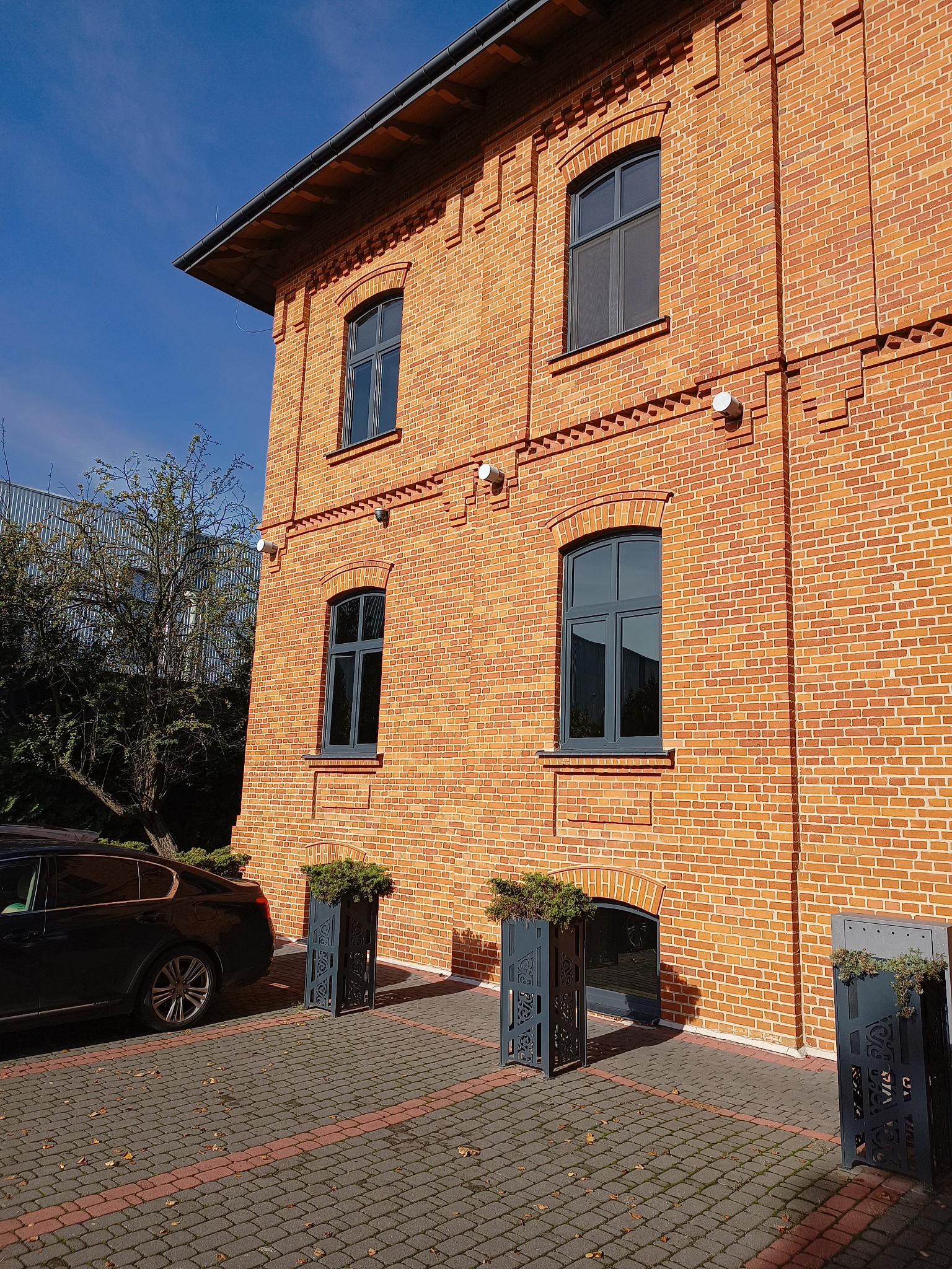 Odrestaurowana kamienica z czerwonej cegły z szarymi oknami i dekoracyjnymi donicami przy wejściu, widok z dołu w słoneczny dzień.