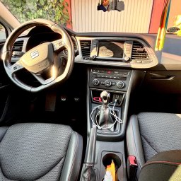 Parowy Marcin mobilna myjnia parowa Marcin Musiałowski - Wnętrze samochodu marki Seat z widoczną deską rozdzielczą, kierownicą i fotelami z czarną tapicerką i czerwonymi przeszyciami. W tle widoczne winogrona.