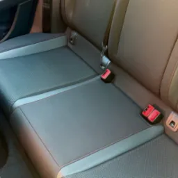 Wnętrze samochodu: tylna kanapa z tapicerką w odcieniach szarości i brązu, z widocznymi elementami mocowania pasów bezpieczeństwa i detalami przeszyć.