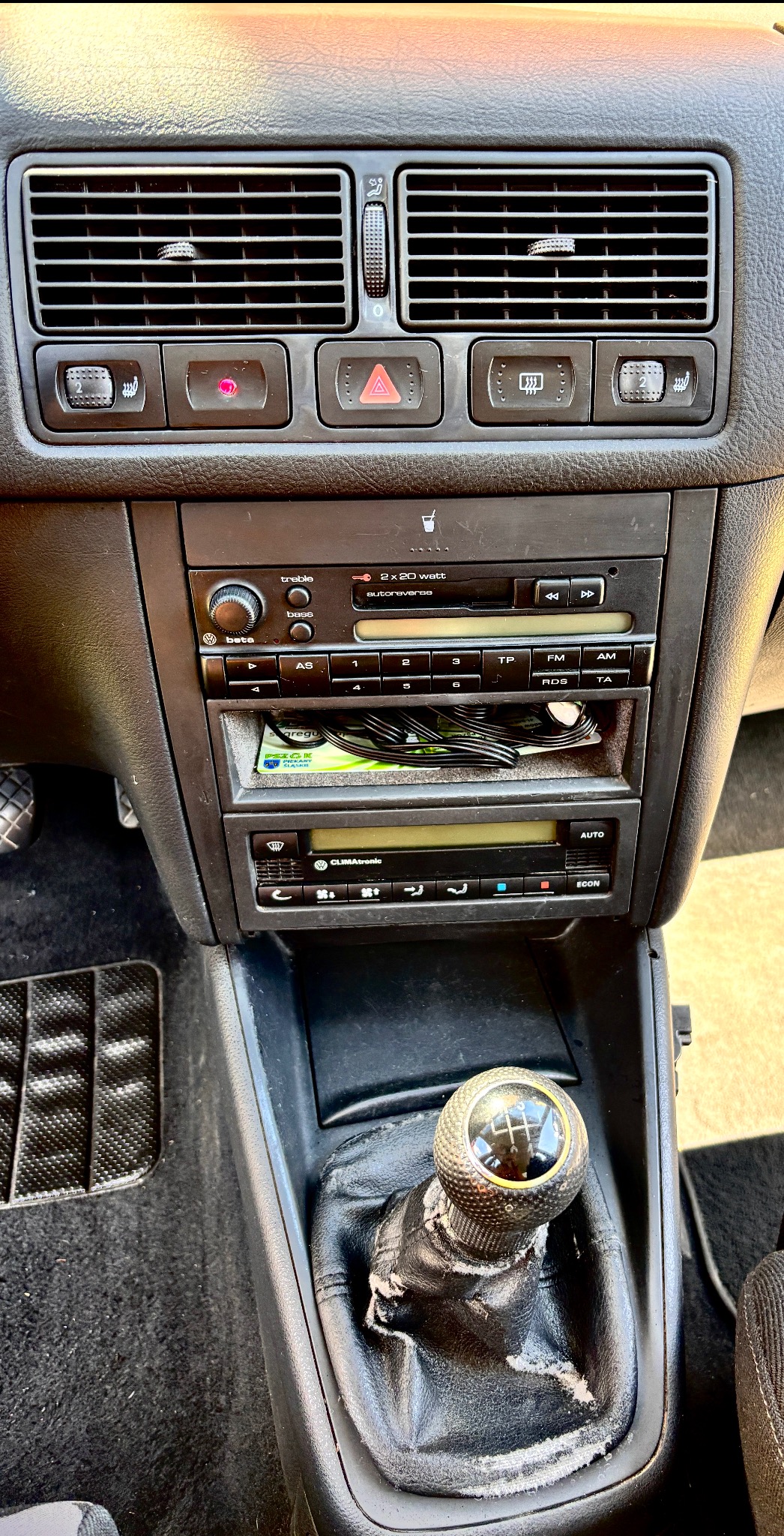 Wnętrze samochodu: deska rozdzielcza z radiem, klimatyzacją i dźwignią zmiany biegów z widocznymi śladami zużycia. Widoczne kratki wentylacyjne i elementy sterujące.