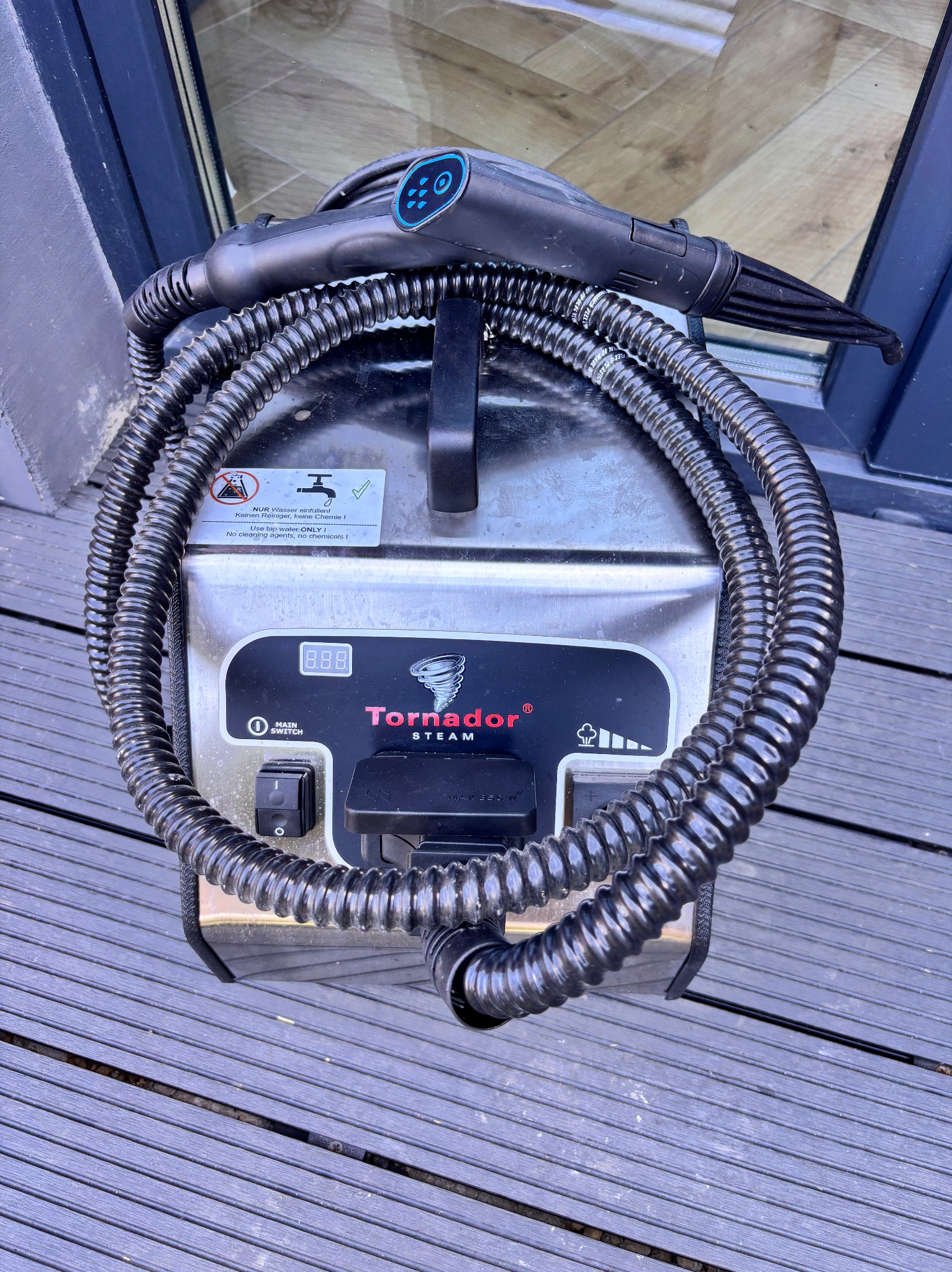 Profesjonalny parowy odkurzacz Tornado Steam z owiniętym wężem, gotowy do czyszczenia tapicerki na tle drewnianej podłogi. Widoczny panel sterowania.