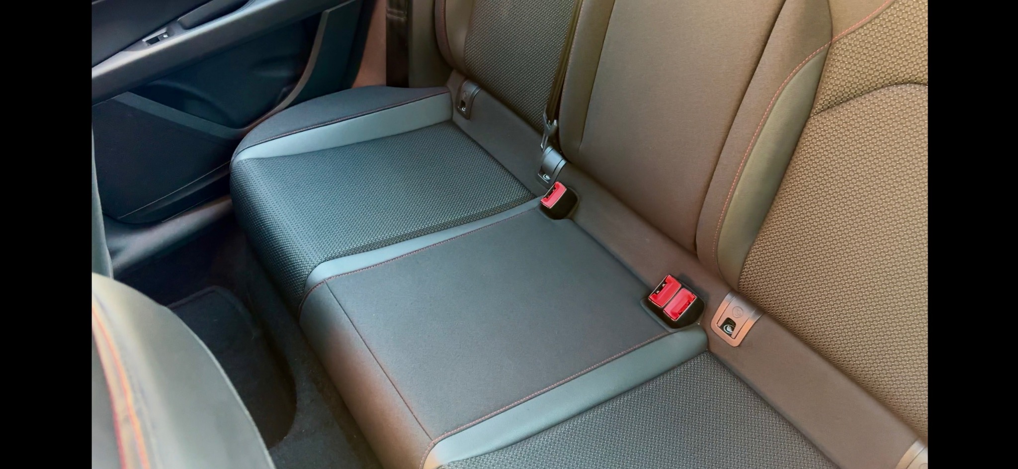 Wnętrze samochodu: tylna kanapa z tapicerką w odcieniach szarości i brązu, z widocznymi elementami mocowania pasów bezpieczeństwa i detalami przeszyć.