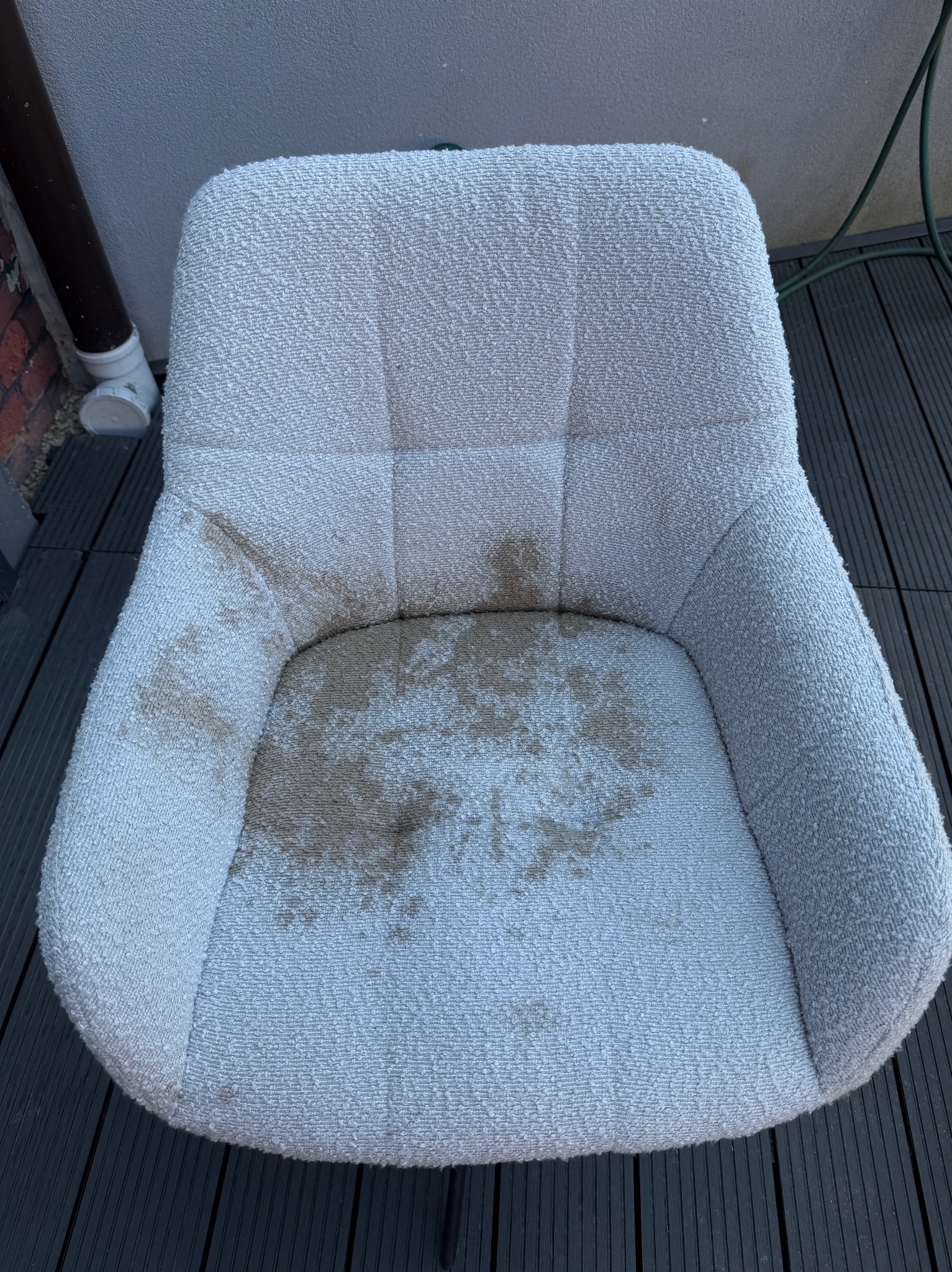 Białe, tapicerowane krzesło z wyraźnymi plamami na siedzisku, stojące na ciemnym tarasie. Widoczny fragment rynny przy ścianie.