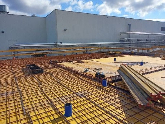 Przygotowanie zbrojenia i szalunku na płycie stropowej budynku przemysłowego, widoczne elementy konstrukcyjne i materiały budowlane na tle hali.