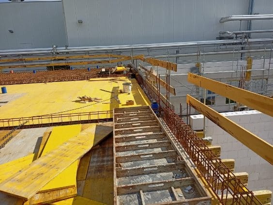 Szare szalunki pod budynek żelbetowy z żółtymi elementami, widoczna stal zbrojeniowa wzdłuż krawędzi.