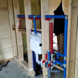 JAS-PRO Piotr Jaśkiewicz - Instalacja podtynkowa WC w drewnianej konstrukcji szkieletowej. Widoczne rury doprowadzające wodę (czerwone i niebieskie) oraz odpływ kanalizacyjny.