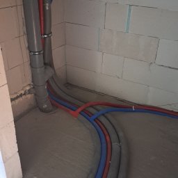 InstalHydroMax - Szare, czerwone i niebieskie rury instalacji grzewczej ułożone w surowym pomieszczeniu z białymi ścianami z betonu komórkowego, widok z góry.
