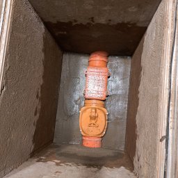 InstalHydroMax - Pionowo zamontowane dwa pomarańczowe elementy rewizyjne instalacji kanalizacyjnej, osadzone w prostokątnym, surowym kanale z betonowymi ścianami i wilgotnym dnem.