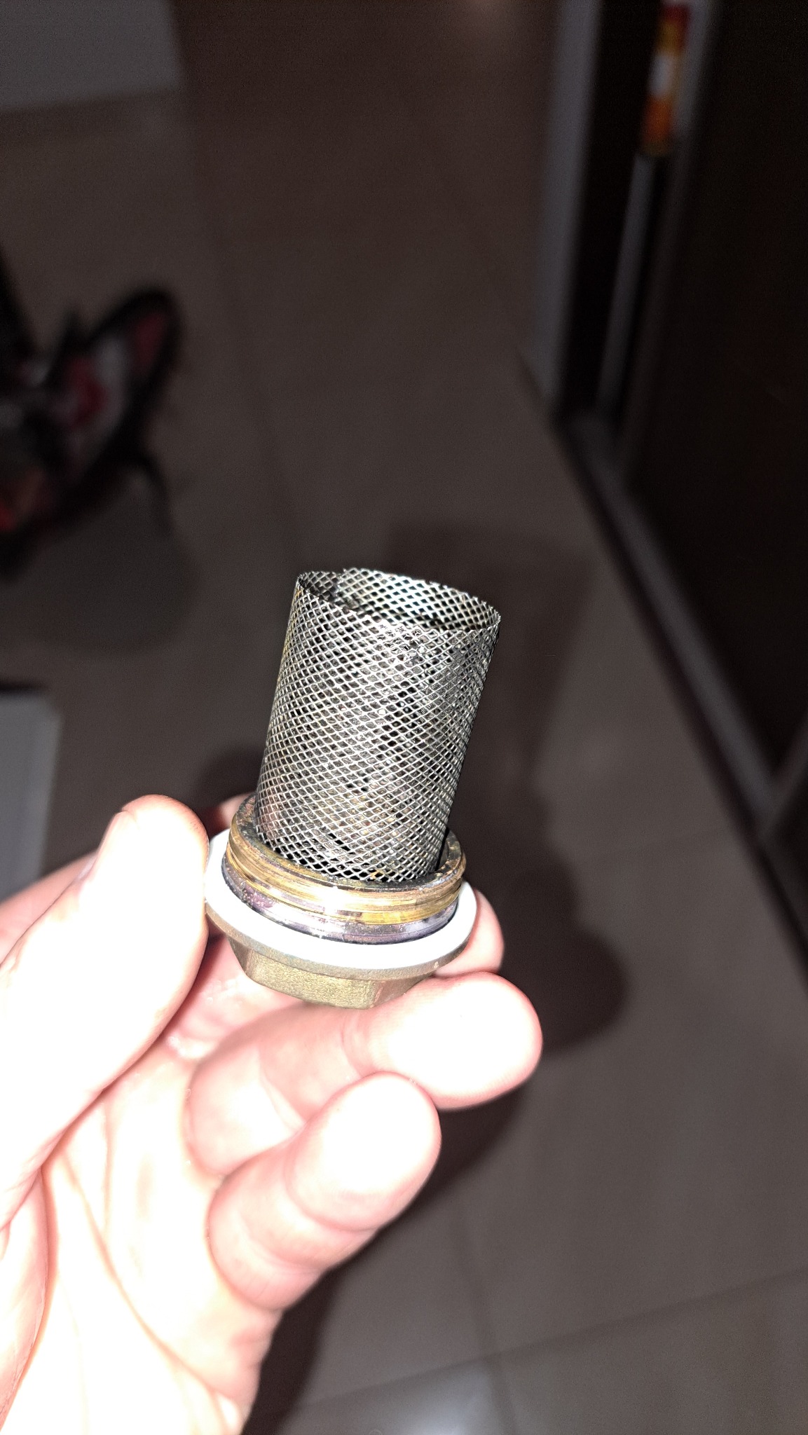 Zanieczyszczony filtr siatkowy w dłoni, element instalacji hydraulicznej. Widoczne osady i zabrudzenia na metalowej siatce. Ujęcie z bliska, ciemne tło.