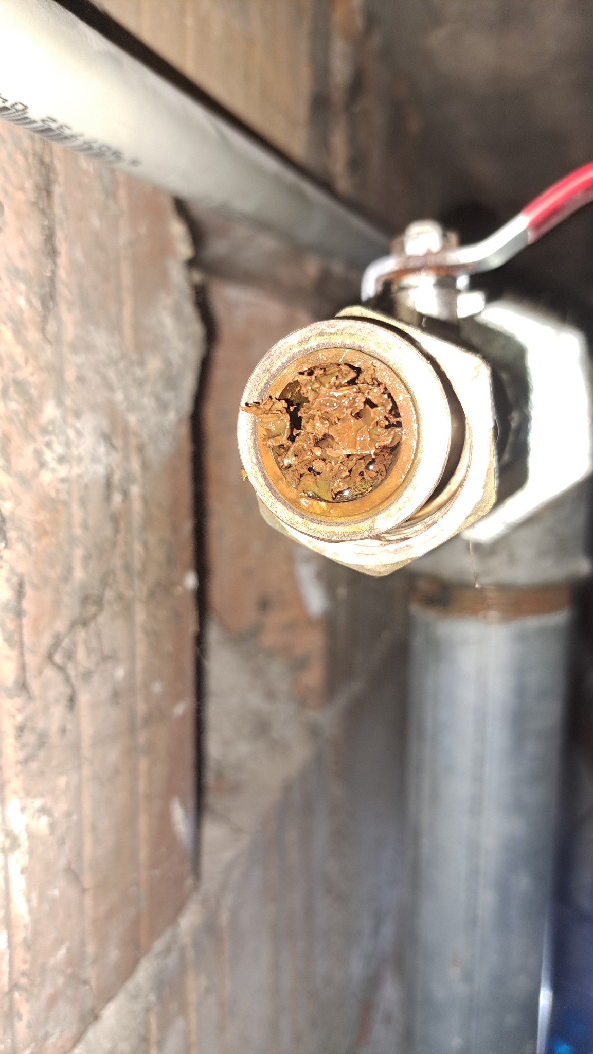 Zardzewiały zawór odcinający z widocznym osadem i korozją wewnątrz, zamontowany przy ścianie z cegieł. Widoczny fragment rury i instalacji.