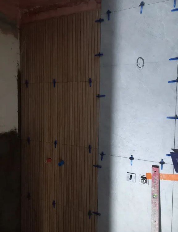 Układanie płytek imitujących drewno na ścianie w Kielcach, z użyciem systemu poziomowania płytek i poziomicy, widoczne gniazdka elektryczne.