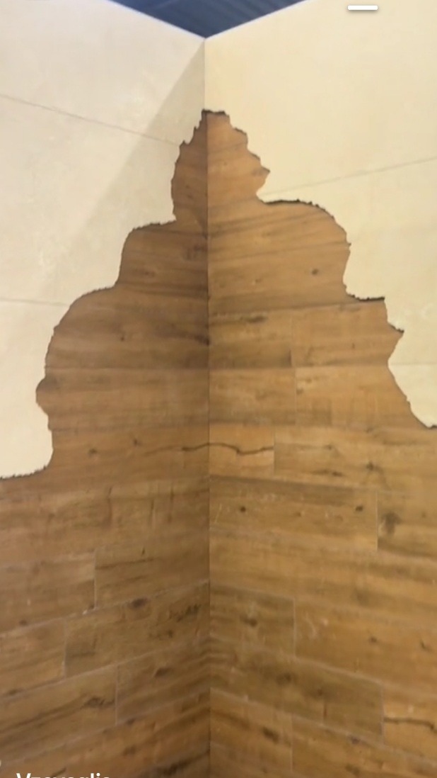 Fragment ściany narożnej z częściowo usuniętą warstwą tynku odsłaniającą imitację drewnianych paneli.