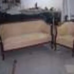 Dwuosobowa sofa i fotel tapicerowane beżową tkaniną, widoczne w warsztacie tapicerskim, po renowacji lub w trakcie naprawy.