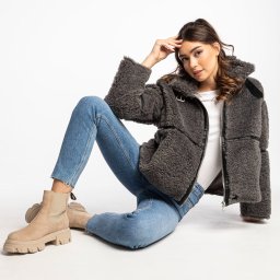 Sylwia Wałęska Photographer - Kobieta w jeansach i kurtce z baranka, siedząca na białym tle, prezentuje modny look z beżowymi botkami na platformie.