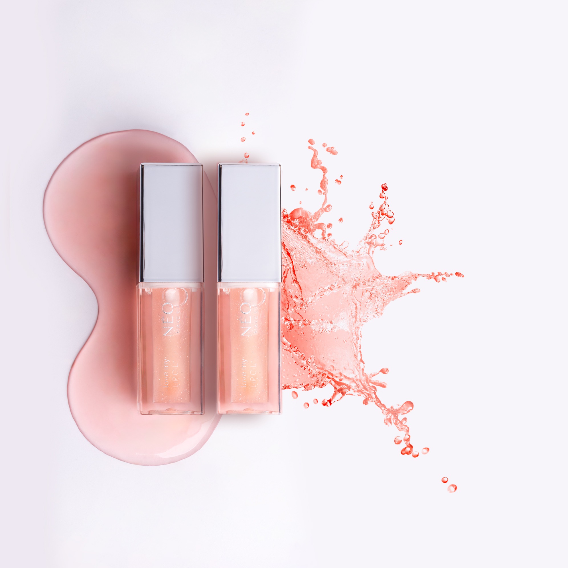 Dwa błyszczyki do ust marki NEO na białym tle z różową plamą i rozpryskiem. Błyszczące, srebrne nakrętki. Minimalistyczna fotografia produktowa.
