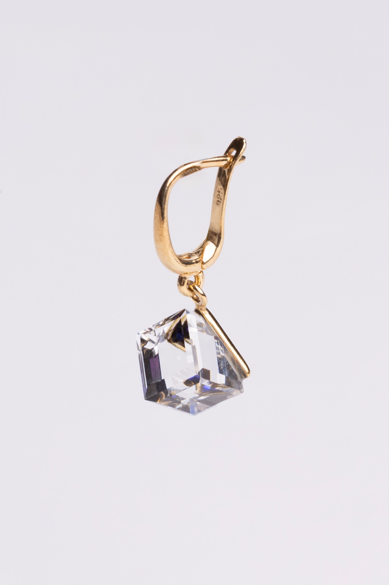 Złoty kolczyk z kryształem o fasetowanym szlifie, zawieszony na tle jasnego studia. Widoczne oznaczenie próby złota '925'.