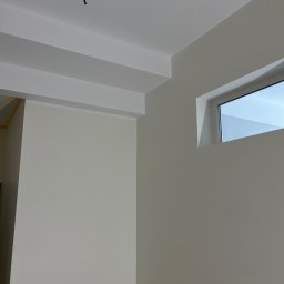 Roman Horditsa - Wnętrze pokoju po malowaniu na jasny odcień beżu, widoczne fragmenty sufitu z listwami dekoracyjnymi, okno oraz wystające kable.