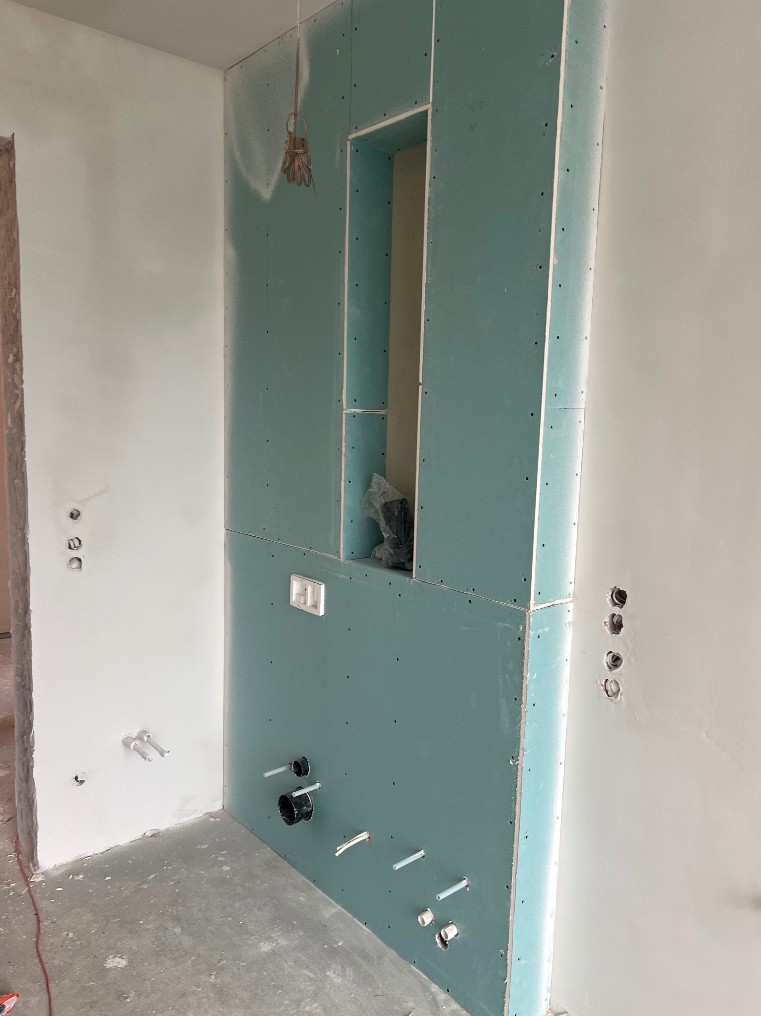 Ściana w trakcie zabudowy z płyt kartonowo-gipsowych z wnęką i instalacją hydrauliczną, widoczne otwory na gniazdka elektryczne oraz wystające rury.