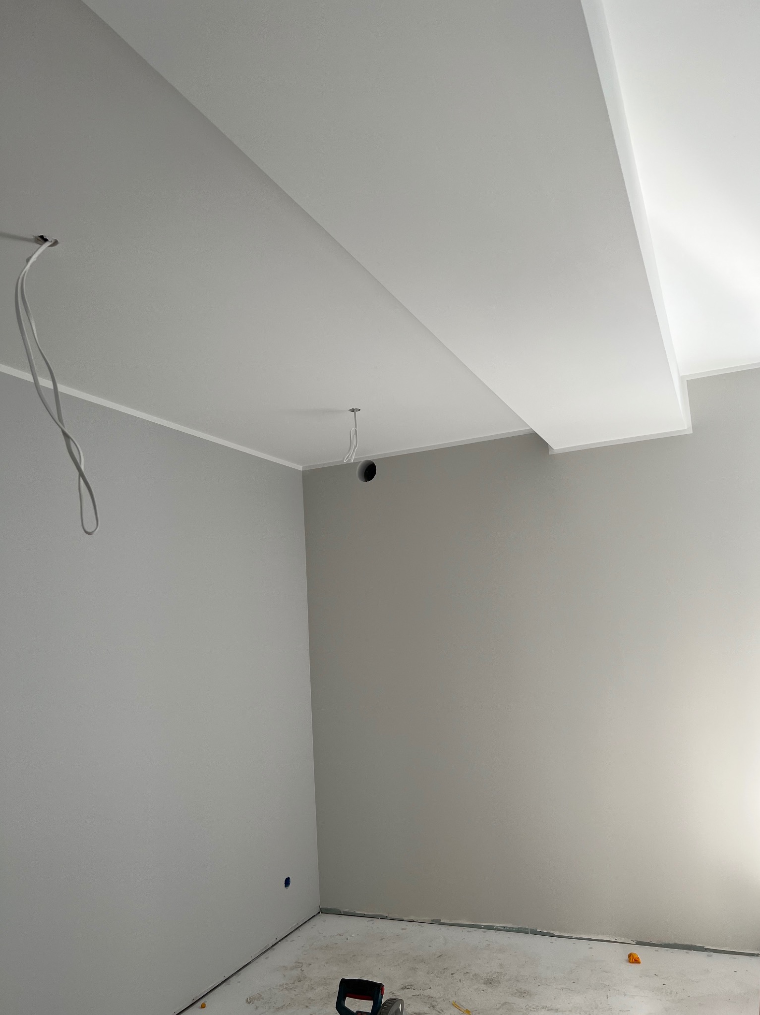 Świeżo pomalowane na szaro wnętrze z białym sufitem podwieszanym i wystającymi kablami elektrycznymi, widoczne ślady po pracach na podłodze.