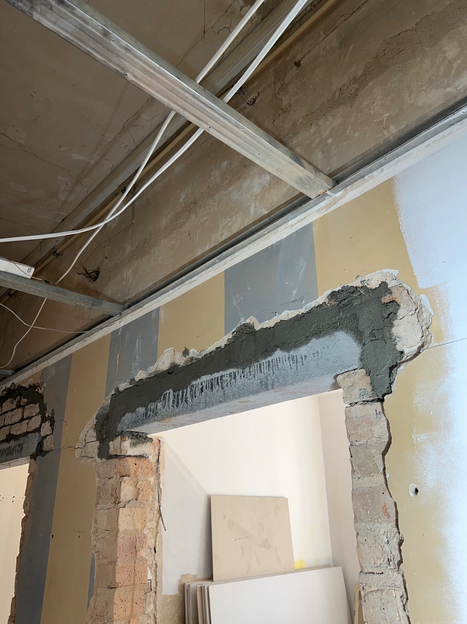 Przygotowanie otworu drzwiowego: obramowanie z cegły z nałożoną zaprawą, widoczne płyty kartonowo-gipsowe i metalowy stelaż pod sufitem.