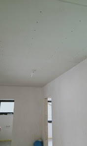 Biały sufit z widocznymi śladami po szpachlowaniu, przygotowany do dalszych prac wykończeniowych. W tle widoczne okno i fragment pomieszczenia.