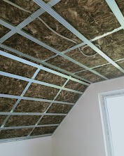 Skośny sufit poddasza z metalowym stelażem i ociepleniem z wełny mineralnej, przygotowany do montażu płyt karton-gips. Widoczny fragment ściany i okna.