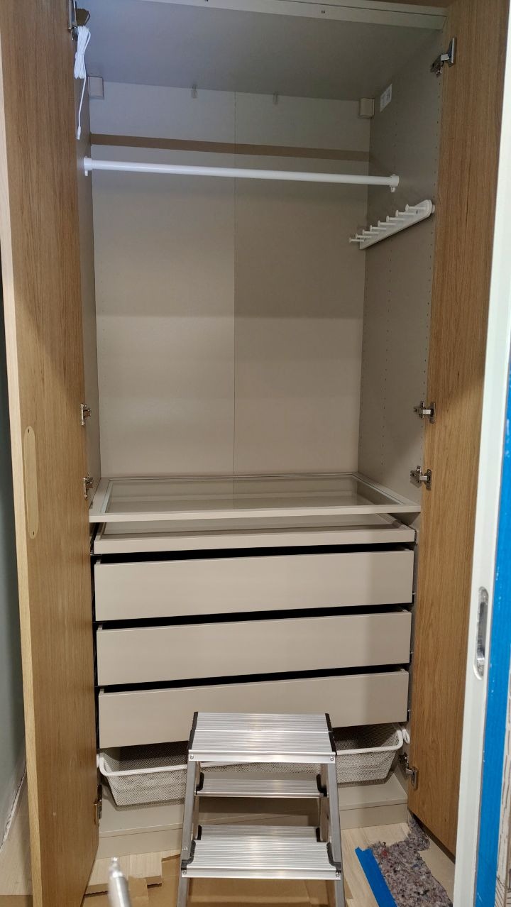 Wnętrze szafy z zamontowanymi szufladami, półkami i drążkiem na ubrania, widoczna aluminiowa drabinka pomocnicza.