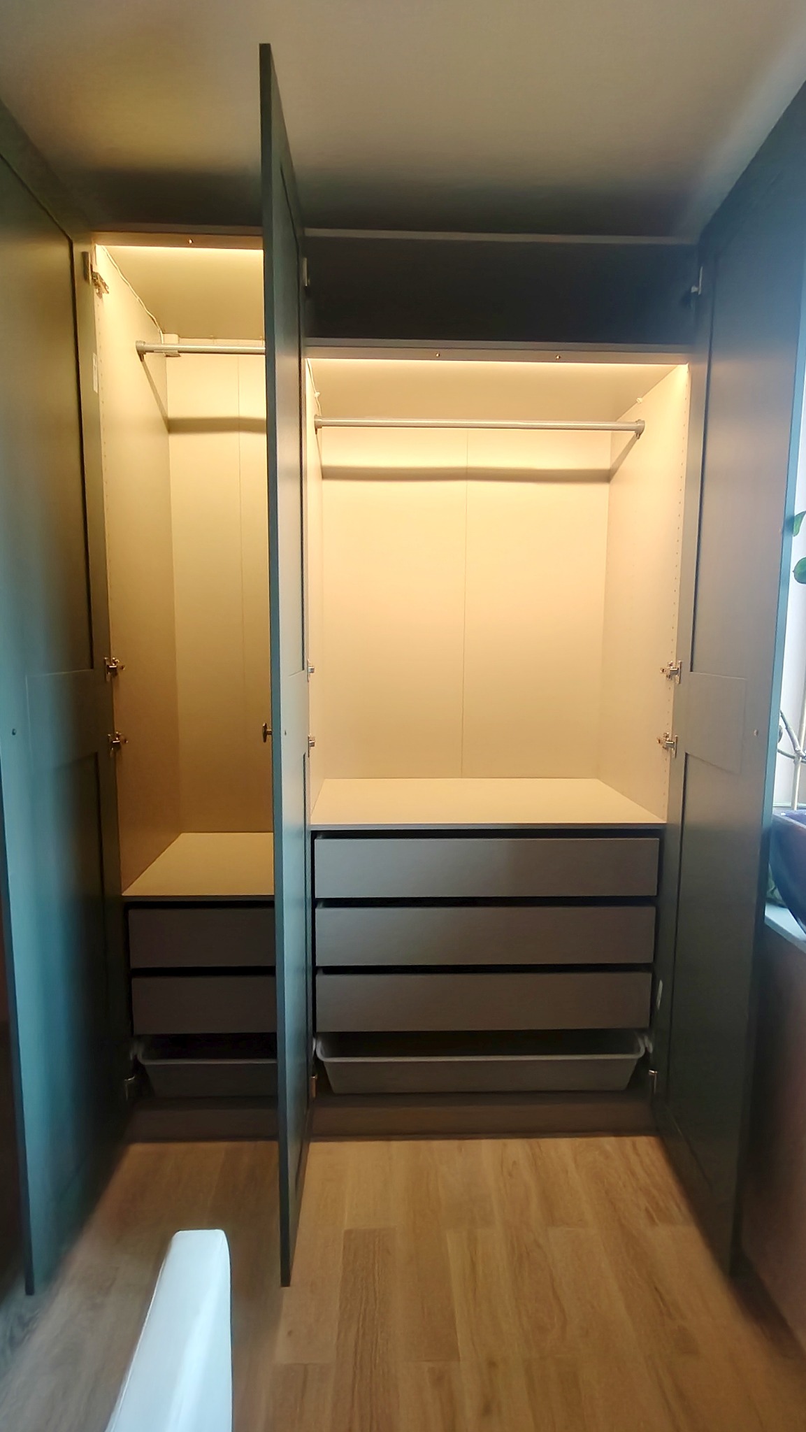 Wnętrze szafy wnękowej z oświetleniem LED, widoczne półki, szuflady i drążek na ubrania, fronty w kolorze ciemnej zieleni, otwarte drzwi ukazują jasne wnętrze.