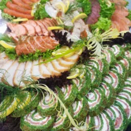 Dekoracyjna taca z różnorodnymi przystawkami rybnymi: roladki ze szpinaku i łososia, wędzone ryby w plastrach, plastry łososia, dekorowane sałatą, koperkiem i cytryną.