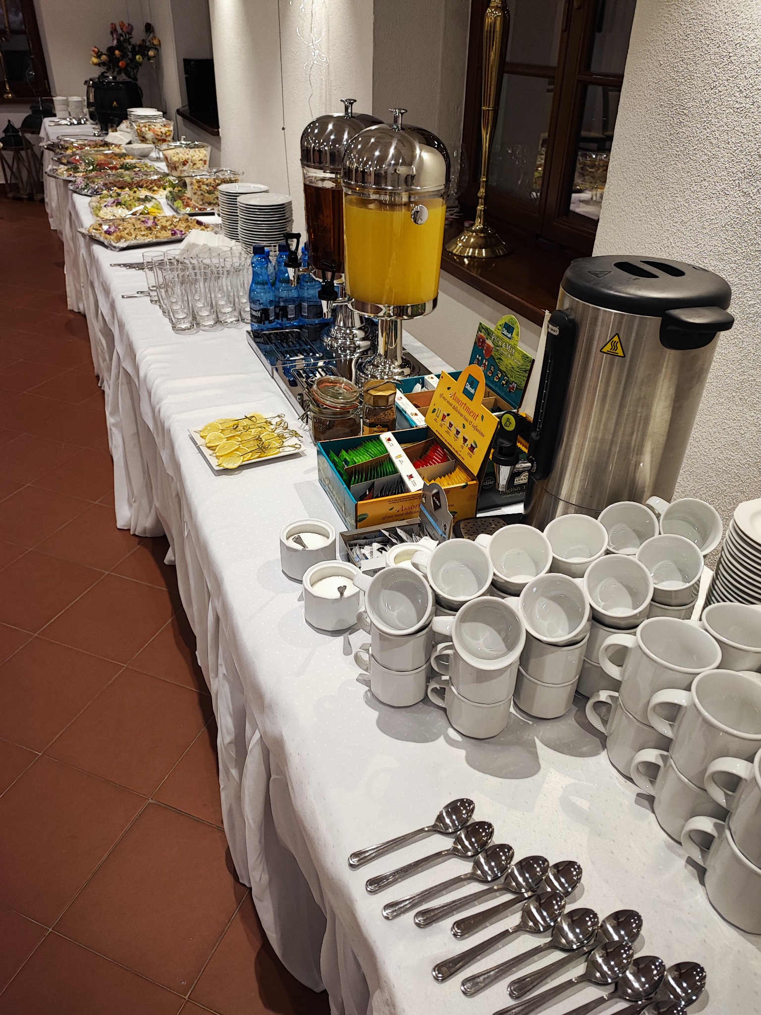 Stół bufetowy z napojami w dystrybutorach, przekąskami, filiżankami, herbatami i cytrynami, przygotowany na wydarzenie.