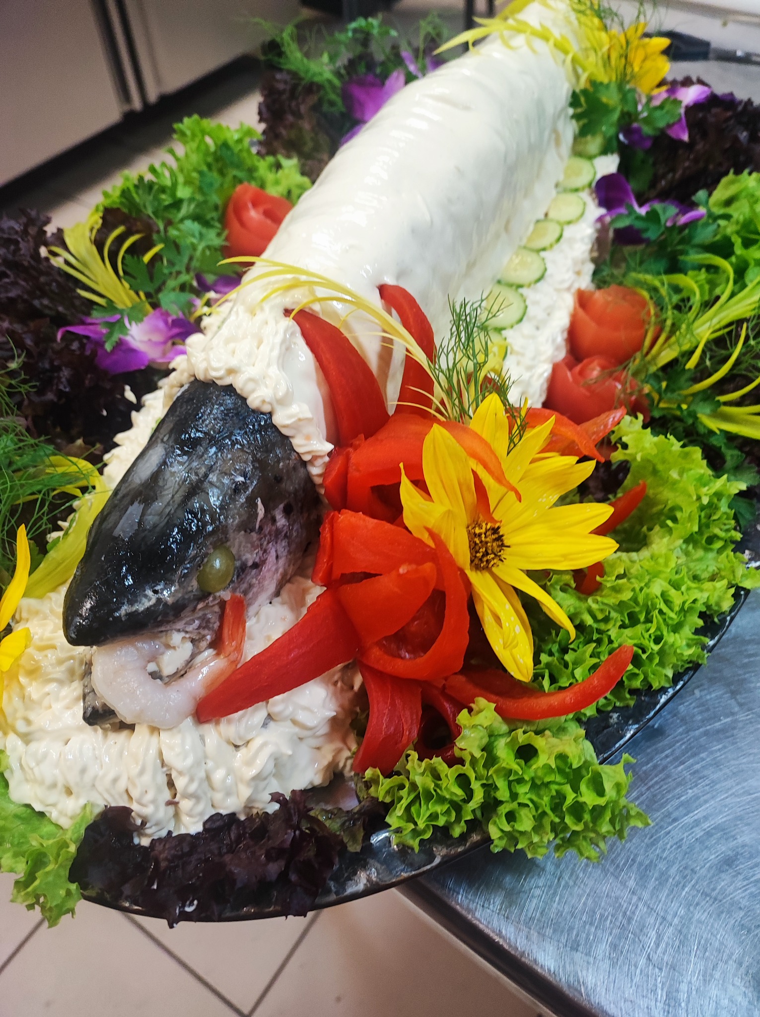 Dekoracyjna ryba w galarecie, ozdobiona warzywami, kwiatami i krewetkami, na czarnym talerzu.