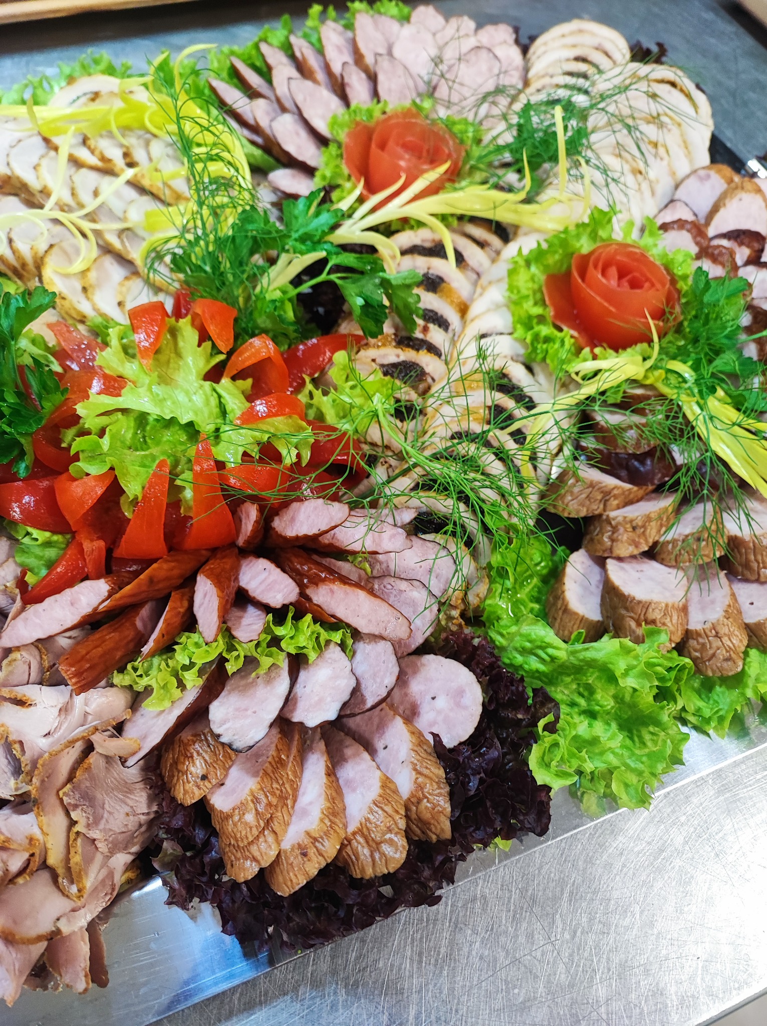 Dekoracyjna taca z różnorodnymi wędlinami, udekorowana sałatą, papryką i koperkiem, tworząc kompozycję z elementami kwiatowymi z warzyw.