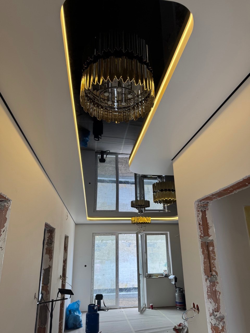 Czarny, błyszczący sufit z oświetleniem LED i ozdobnym żyrandolem w przestronnym wnętrzu w trakcie wykończenia. Widok z dołu.
