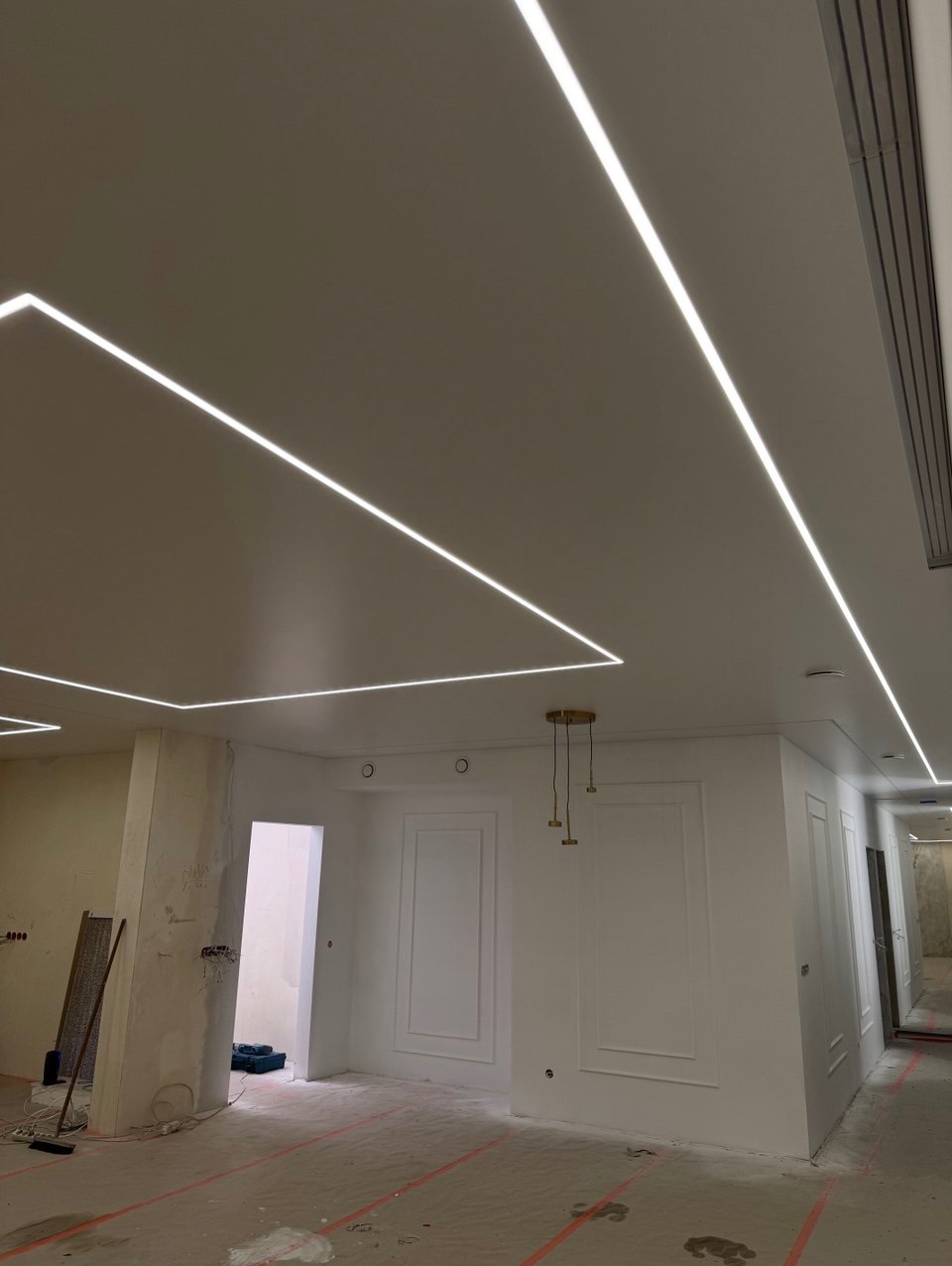 Sufit napinany z liniowym oświetleniem LED w kształcie prostokątów. Widoczne przygotowania do dalszych prac wykończeniowych w pomieszczeniu.