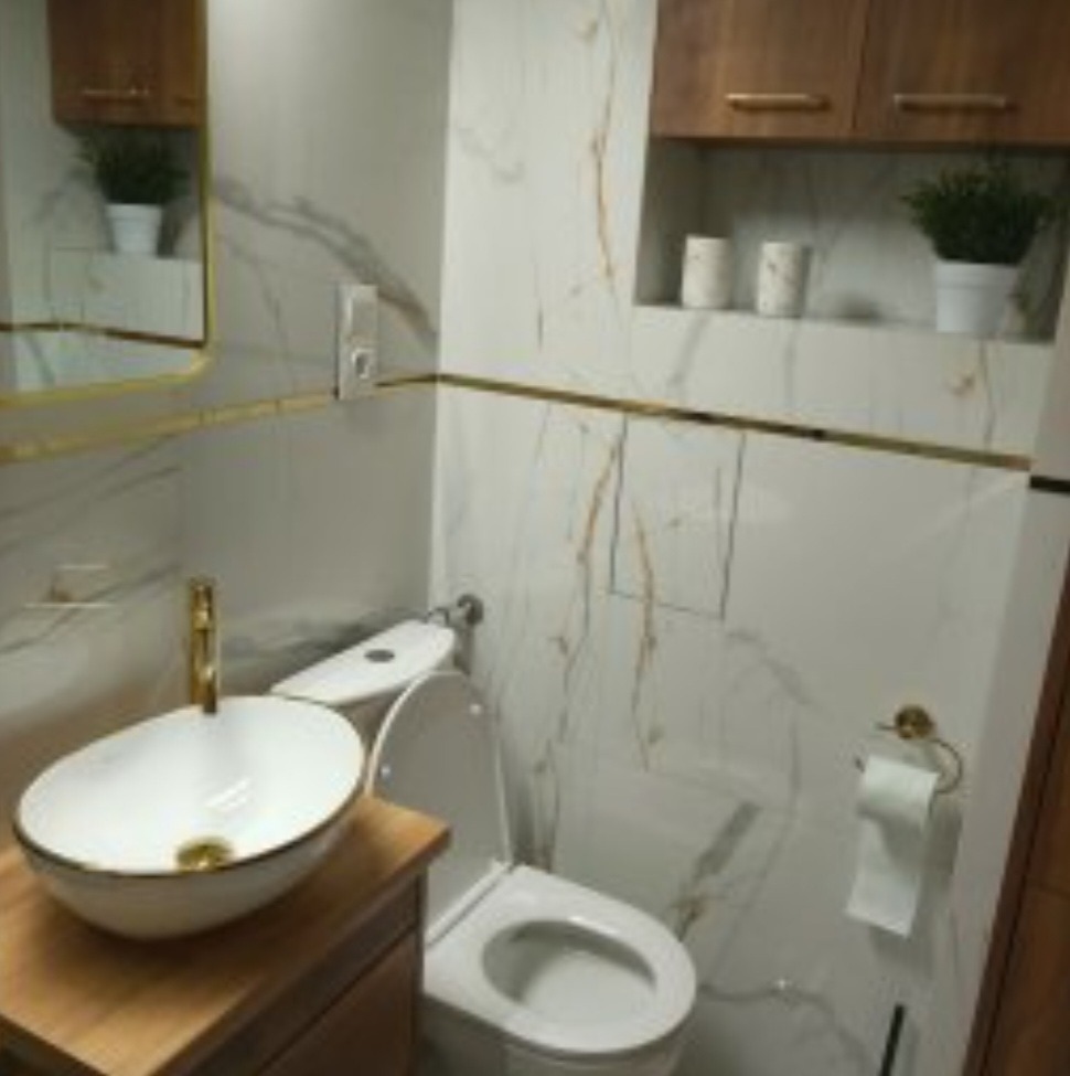 Nowoczesna łazienka z marmurowymi płytkami, złotymi akcentami i umywalką nablatową na drewnianej szafce.