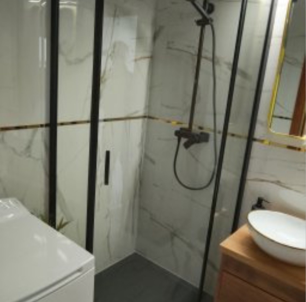 Wykończona łazienka z kabiną prysznicową typu walk-in z czarnymi profilami, marmurowe płytki, umywalka nablatowa na drewnianej szafce.