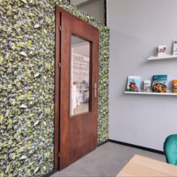 Wnętrze biura ubezpieczeniowego z zieloną ścianą, drewnianymi drzwiami z napisem 'Biuro Rachunkowe Ubezpieczenia' i półkami z broszurami informacyjnymi.