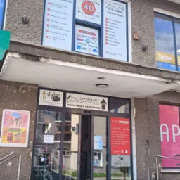 Fasada budynku z szyldami firm: biuro rachunkowe 'Kraina Podatków', ubezpieczenia, sklepy odzieżowe 'Stylove' i 'Modny Elegancik' oraz 'Home Decor'.