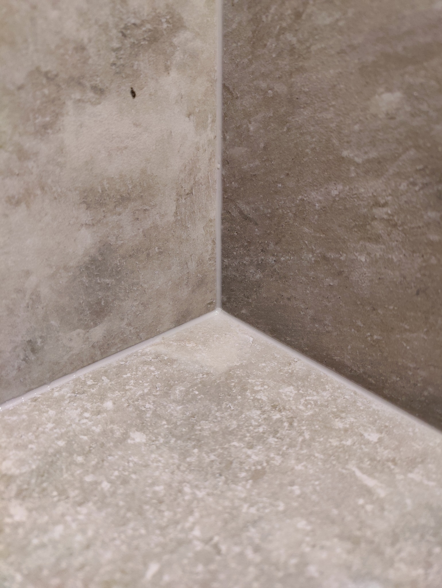Szczegółowe ujęcie narożnika wykończonego płytkami w odcieniach beżu i szarości, z wyraźnie widoczną fugą i delikatną strukturą kamienia.