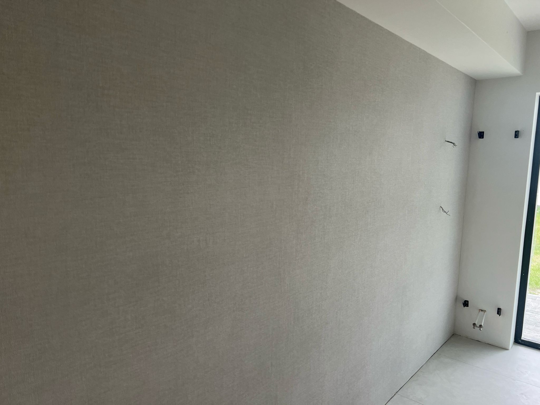 Gładka, szara ściana z fakturą w nowym wnętrzu, z widocznymi przewodami i instalacją. Minimalistyczny design, świeżo po malowaniu.