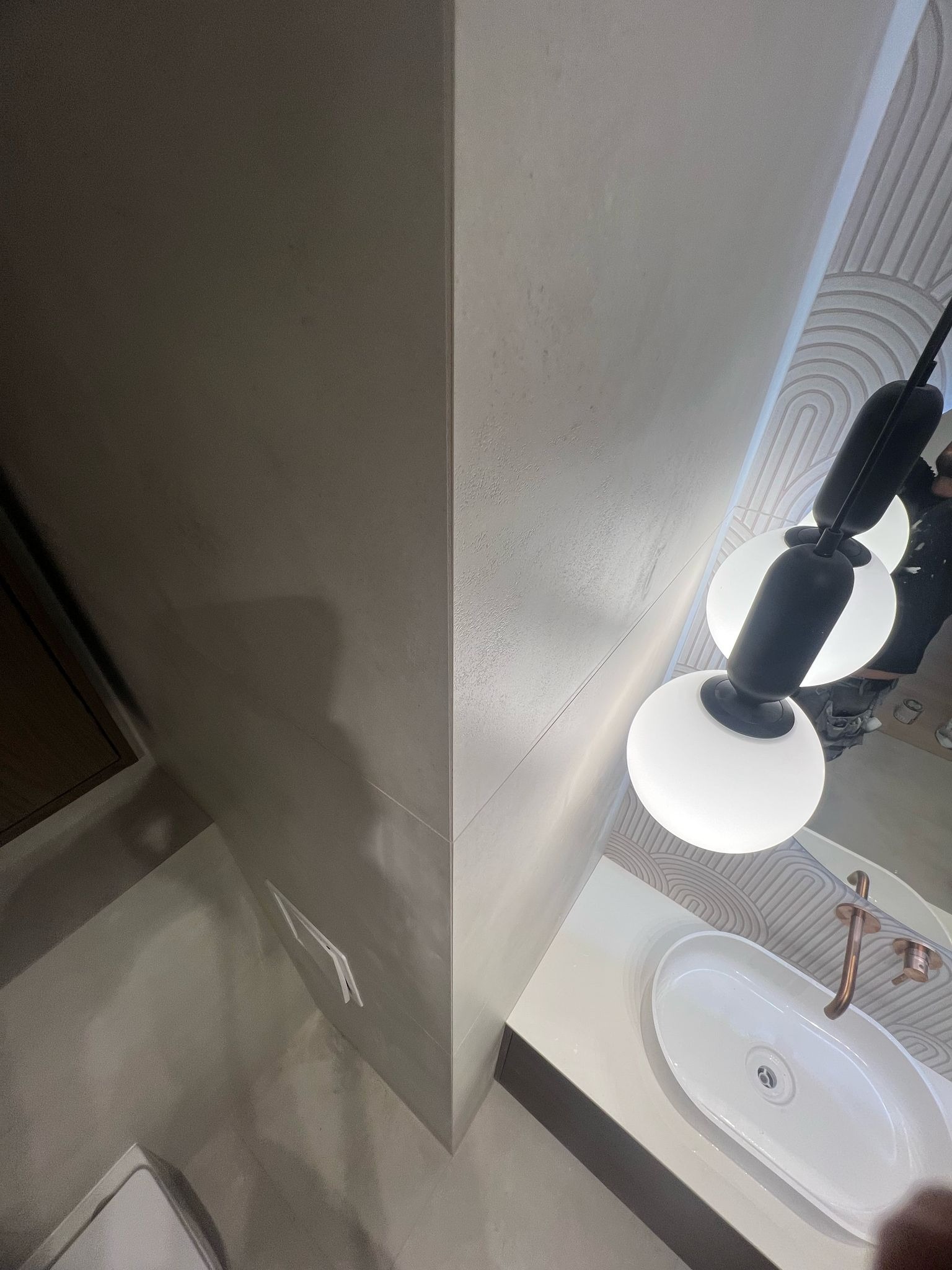 Nowoczesna łazienka z umywalką nablatową, ozdobną armaturą i geometrycznym wzorem na ścianie, oświetlona kulistą lampą. Minimalistyczny design.