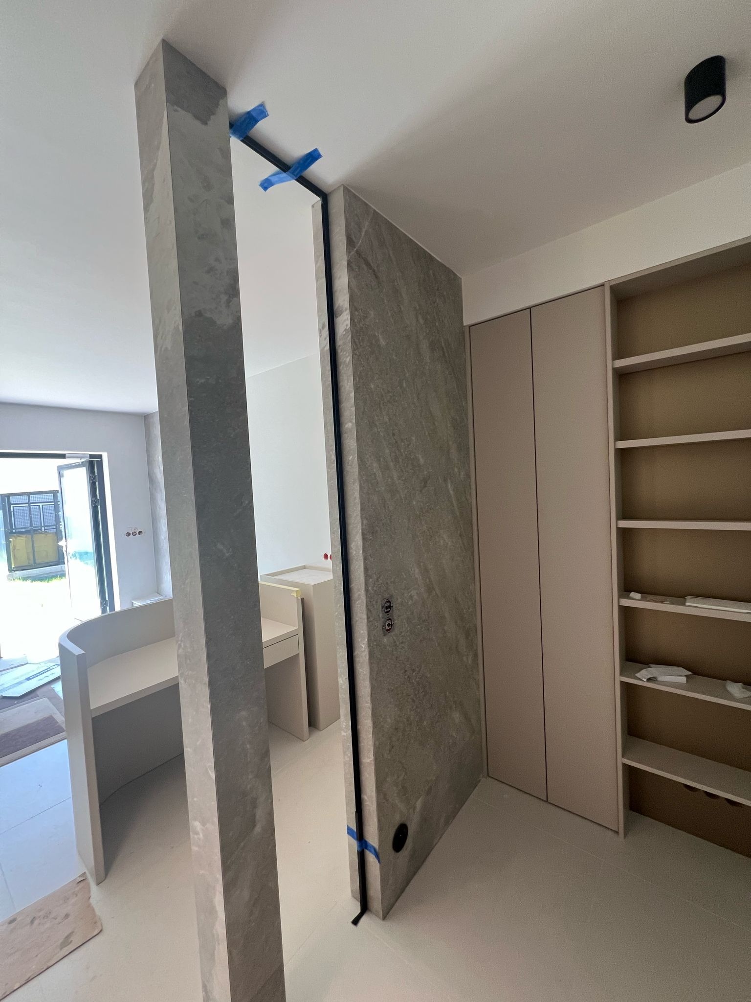 Wnętrze w trakcie remontu: kolumna i ściana wykończone płytami imitującymi kamień, zabudowa meblowa w jasnych odcieniach. Prace wykończeniowe w nowoczesnym stylu.