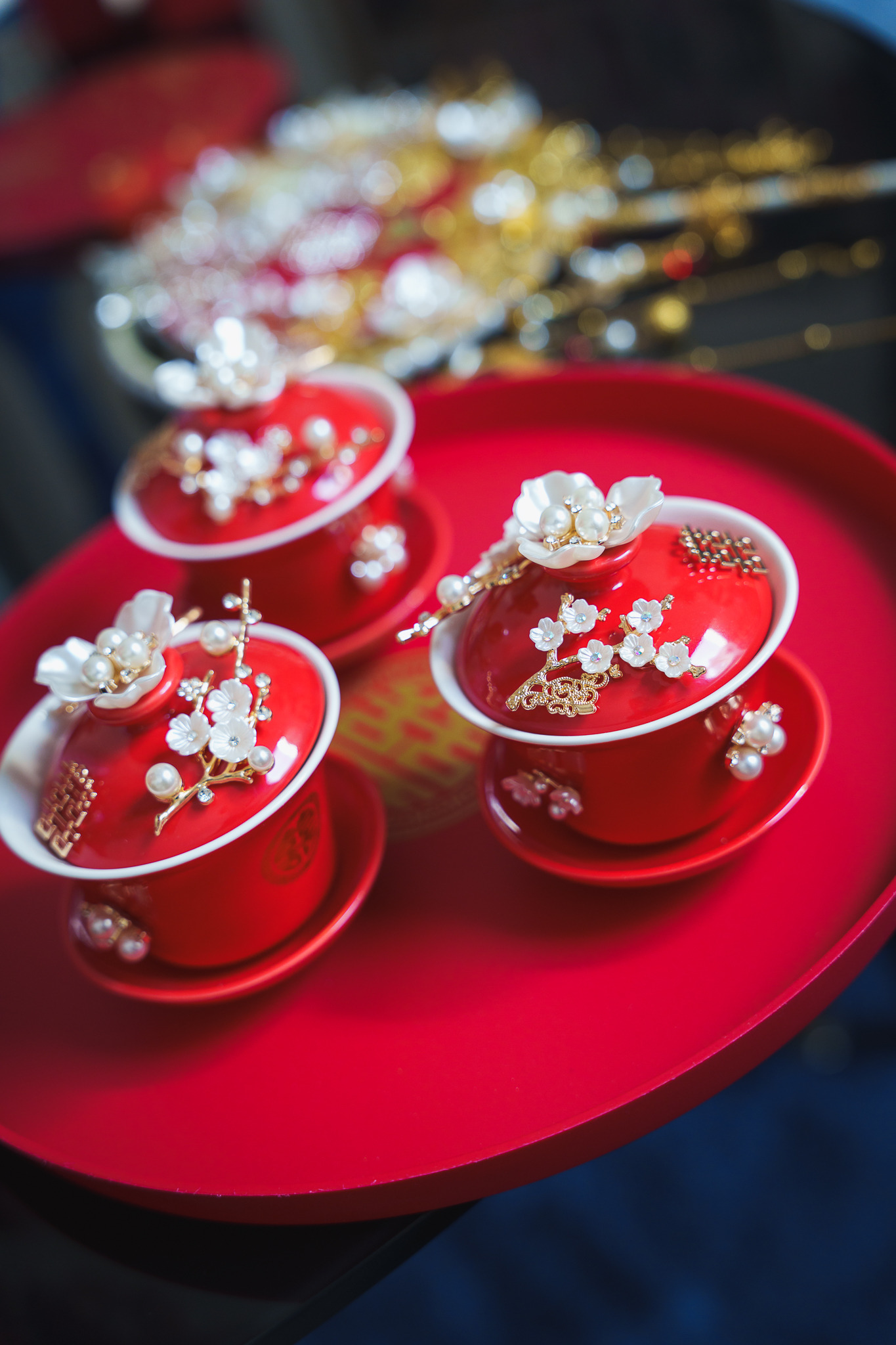 Trzy czerwone, zdobione czarki na czerwonej tacy. Dekoracje kwiatowe z perłami i złotymi elementami. Tradycyjna ceremonia ślubna, detale.