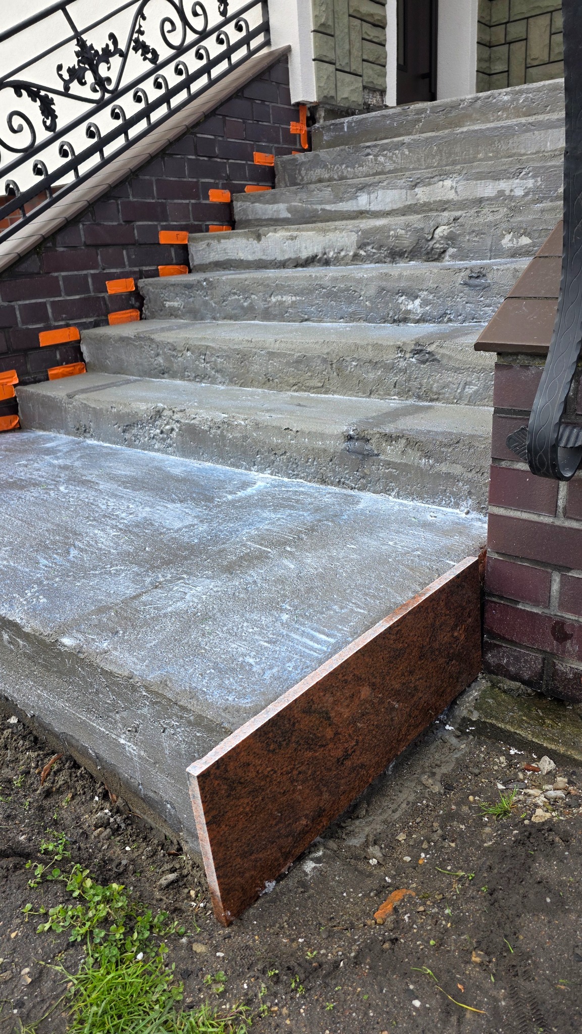 Betonowe schody zewnętrzne w trakcie wykończenia, z widocznymi elementami montażowymi i fragmentem okładziny kamiennej na pierwszym stopniu.